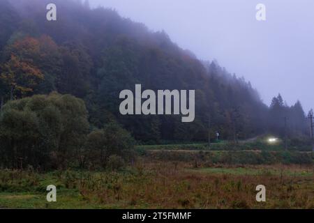 Misty Morning nelle montagne autunnali. Luci per auto nella nebbia sulla strada in montagna. Viaggia nella nebbia. Paesaggio misterioso nelle montagne dei Carpazi. Foto Stock