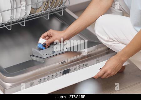 la mano femminile consente di aprire la lavastoviglie automatica incorporata con il piatto sporco all'interno. Primo piano Foto Stock