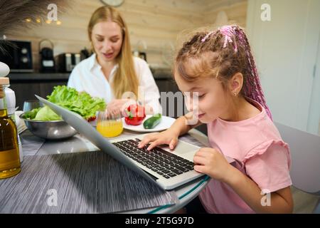 Piccola studentessa che studia online o fa il suo lavoro a casa con un computer portatile Foto Stock