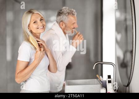 Rituali mattutini. Coppia matura felice che fa la routine self-care vicino allo specchio in bagno Foto Stock