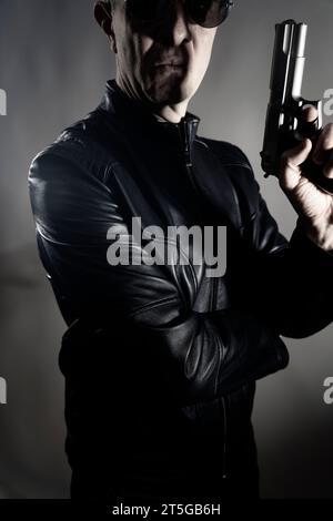 Giacca nera in pelle assassino detective spia assassino assasin con foto ritratto a pistola. Foto Stock