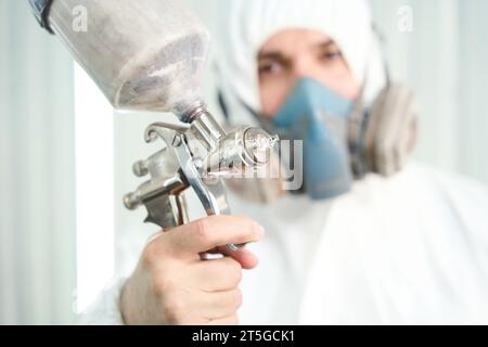 Un pittore esperto in indumenti protettivi utilizza uno strumento di verniciatura Foto Stock