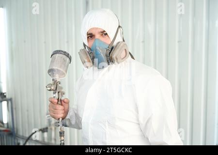 Pittore industriale serio con strumento di verniciatura in piedi in un'officina di riparazione Foto Stock