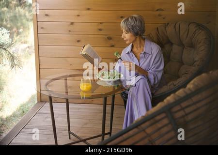 Una donna anziana in abiti lilla si siede sulla terrazza Foto Stock