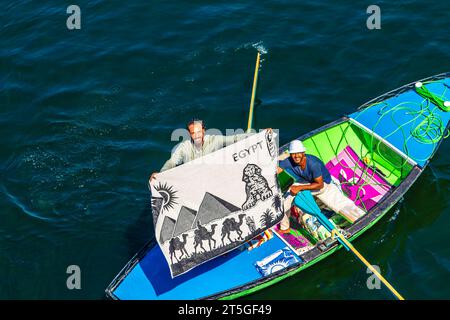 I venditori di tessuti sulle loro barche si avvicinano a una nave da crociera in attesa di entrare nella chiusa di Esna. I venditori sperano di vendere beni ai turisti. Esna, Egitto – 20 ottobre Foto Stock