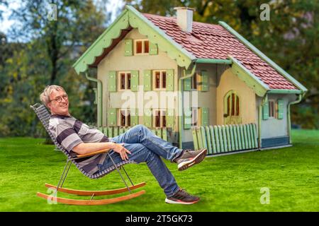 älterer Mann sitzt entspannt vor seinem Haus, Symbolfoto Immobilie als Altersvorsorge, 2023 Deutschland, München, November 2023, älterer Mann sitzt zufrieden im Schaukelstuhl vor seinem Haus, Symbolfoto Immobilien als Altersvorsorge, Vermögen, Lebensabend, Sicherheit, Erbe, erben, Haus der Eltern, Glück im Alter, Rentner, Senior, Senioren, vorsorgen, *** uomo anziano seduto rilassato di fronte alla sua casa, foto simboliche immobili come previdenza, 2023 Germania, Monaco di Baviera, novembre 2023, anziano seduto tranquillamente su una sedia a dondolo di fronte alla sua casa, foto simboliche immobili AS Foto Stock