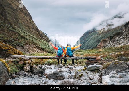 Coppia di escursionisti seduti su un ponte di legno sul percorso di trekking di Mera Peak vicino a Kothe. Uomo e donna sollevano con gioia le braccia. Si divertono con Makalu Barun N. Foto Stock