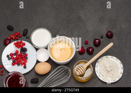 Frusta, ciotola di uova rotte. Farina, latte di bacche, burro, marmellata di miele. Ingredienti per cucinare la colazione. Copia spazio. Spianatura piatta Foto Stock