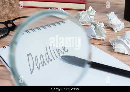 Lente d'ingrandimento su blocco note con termine e sfondo di carta spazzatura sulla scrivania dell'ufficio. Concetto aziendale. Foto Stock