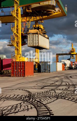 Una gru industriale che solleva le scatole di container per la spedizione e le carica sui carrelli per il trasporto su strada nel Regno Unito e nel mondo Foto Stock