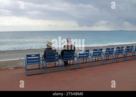 Turisti invernali seduti sulle famose sedie blu della Promenade des Anglais a Nizza Foto Stock