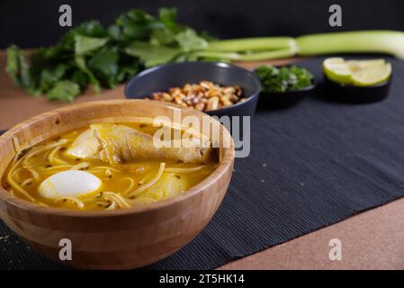Piatto tipico peruviano noto come zuppa di pollo, in una ciotola di legno con limone e erba cipollina. Foto Stock