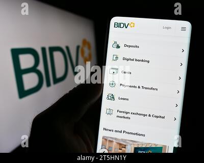 Persona in possesso di cellulare con pagina Web della Banca commerciale per gli investimenti e lo sviluppo del Vietnam con logo. Concentrarsi sul centro del display del telefono. Foto Stock