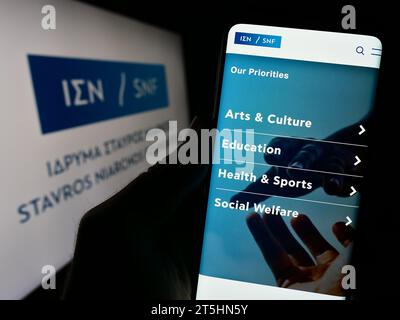 Persona in possesso di cellulare con sito web di orgsniation greca Stavros Niarchos Foundation (SNF) davanti al logo. Concentrarsi sul centro del display del telefono. Foto Stock