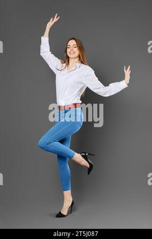 Donna sorridente e gioiosa che si bilancia su una gamba che le salta le braccia Foto Stock