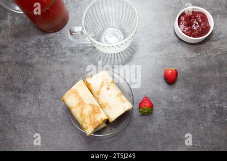 pancake con ripieno di frutti di bosco e fragole, una tazza di tè alla frutta, su un tavolo grigio scuro. vista dall'alto. Foto Stock