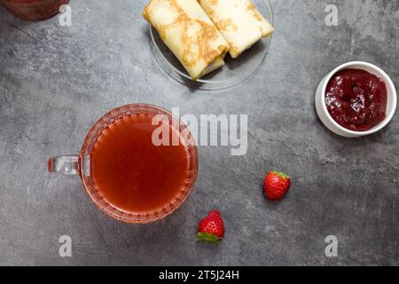 una tazza di tè alla frutta, pancake con ripieno di frutti di bosco e fragole su un tavolo grigio scuro. vista dall'alto. Foto Stock