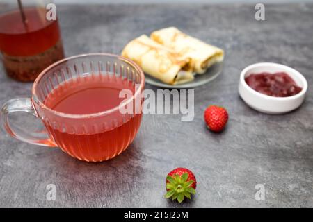 una tazza di tè alla frutta, pancake con ripieno di frutti di bosco e fragole su un tavolo grigio scuro. Foto Stock