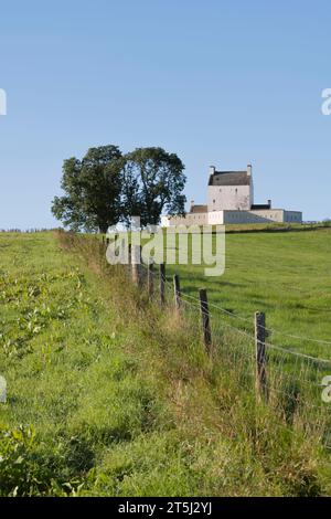 Una recinzione che conduce su una collina a una tribuna di alberi e al Castello di Corgarff nel Parco Nazionale di Cairngorms nel Nord-Est della Scozia Foto Stock