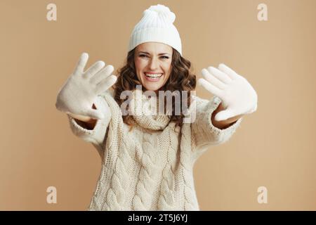 Ciao inverno. donna elegante e sorridente con maglione beige, guanti e cappello isolati su beige. Foto Stock