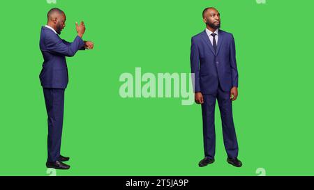 Uomo d'affari che controlla l'ora sull'orologio da polso e aspetta in studio, guarda l'orologio o l'orologio prima di lavorare con una startup. Responsabile aziendale che si pone con fiducia sulla fotocamera. Foto Stock