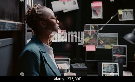 Detective donna che analizza indizi e foto sospette, lavora alla risoluzione del crimine in ufficio. Agente legale che esamina i precedenti penali con esperienza legale, alla ricerca di prove fisiche. Foto Stock