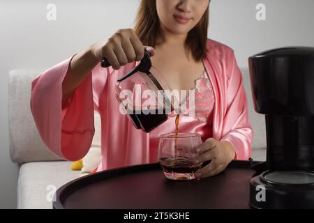 La donna asiatica sta felicemente preparando il caffè nel suo pigiama di raso rosa la mattina. Foto Stock