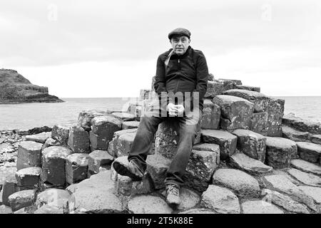 Ritratto di un uomo seduto sulle rocce al Giants Causeway in Irlanda del Nord Foto Stock