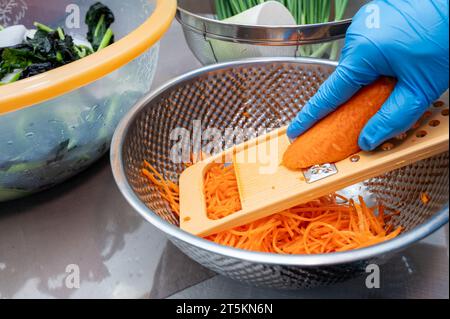 Il processo di preparazione di un piatto tradizionale coreano, il kimchi. Una donna che indossa i guanti sta preparando vari ingredienti necessari per il kimchi. Foto Stock