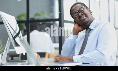 un uomo stanco lavora in un computer in un ufficio di fondo. concetto di problema sul lavoro Foto Stock