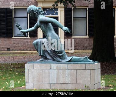 Assen, Paesi Bassi - 11 ottobre 2023 Una statua in bronzo di una figura femminile inginocchiata, con palma d'onore, dello scultore Willem Johannes Valk. E' un monumento Foto Stock