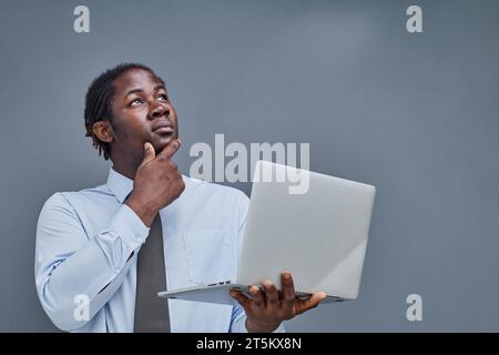 giovane afro-americano su sfondo grigio con in mano un portatile. mostra i pollici in alto Foto Stock