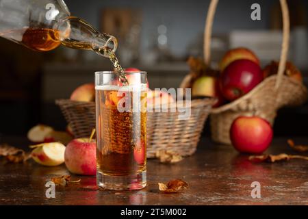 Il sidro di mele viene versato da una bottiglia in un bicchiere. Bevanda fresca con mele su un vecchio tavolo da cucina. Foto Stock