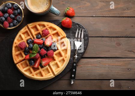 Gustosi waffle belgi con frutti di bosco freschi serviti su un tavolo di legno e piatti. Spazio per il testo Foto Stock