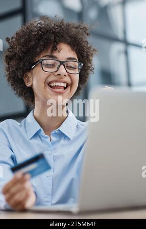 Una ragazza in un ufficio moderno paga gli acquisti su Internet utilizzando una carta di credito Foto Stock