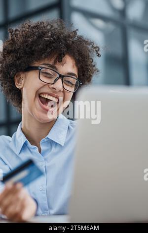 Una ragazza in un ufficio moderno paga gli acquisti su Internet utilizzando una carta di credito Foto Stock