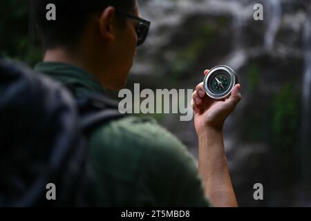 Vista posteriore del viaggiatore maschile con zaino che utilizza la bussola per cercare la direzione durante le escursioni nella foresta Foto Stock