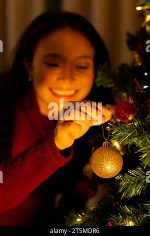 Felice donna asiatica che decora l'albero di natale a casa e sorride Foto Stock
