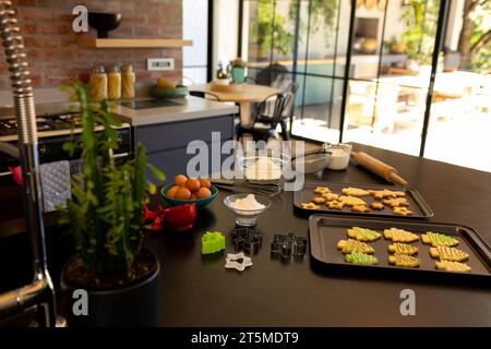 Cucina lussuosa e soleggiata con biscotti di natale appena sfornati in vassoi da forno sul piano di lavoro Foto Stock
