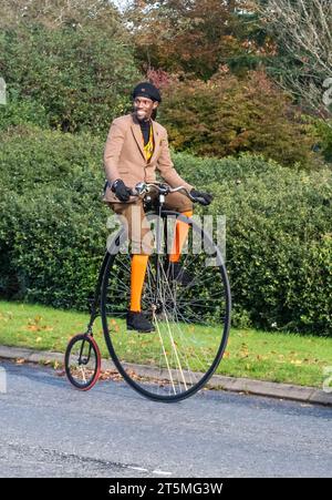 5 novembre 2023. I partecipanti alla corsa di auto da Londra a Brighton Veteran Car Run 2023 guidando attraverso West Sussex, Inghilterra, Regno Unito. Il percorso del famoso evento annuale si estende per 60 chilometri circa. Un uomo che cavalca una bicicletta da un penny. Foto Stock