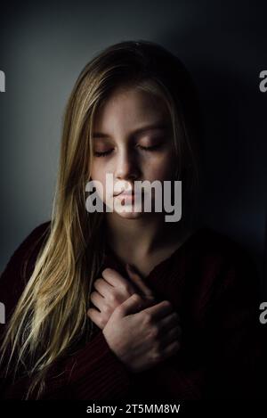 Primo piano di una preadolescente con gli occhi chiusi che tiene la mano su hea Foto Stock