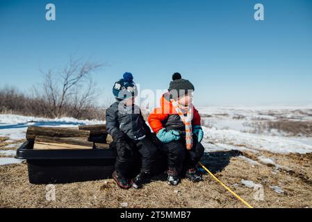 Vista laterale di due bambini seduti su una slitta piena di legna da ardere Foto Stock