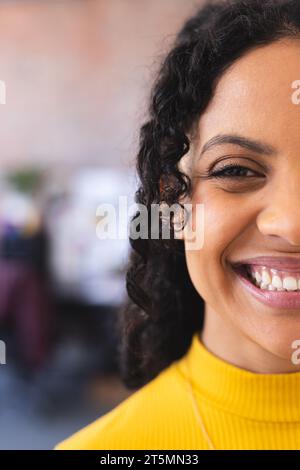 Mezza faccia di felice stilista birazziale in piedi e sorridente in uno studio soleggiato Foto Stock