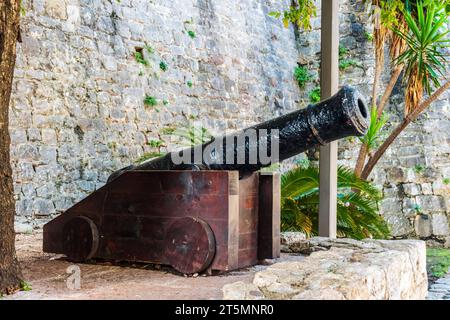 Cannone medievale nella città vecchia di Budva, Montenegro. Botte in ghisa montata su un telaio in legno sullo sfondo di una parete in pietra a Stari Grad Foto Stock