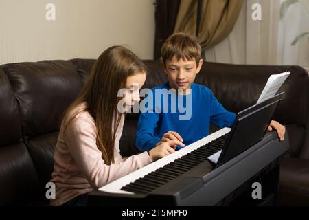 Un ragazzo e una ragazza esercitano il pianoforte insieme in un ambiente caldo e familiare, concentrato e in armonia. Foto Stock