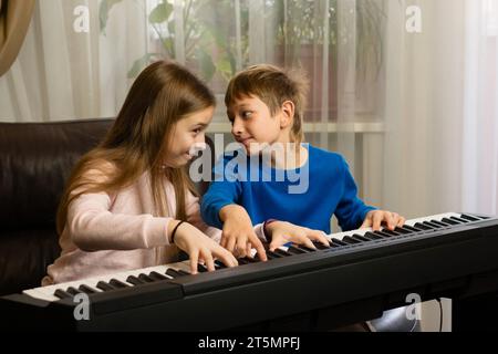 Una ragazza e un ragazzo che praticano il pianoforte insieme, godendosi un momento musicale al chiuso Foto Stock