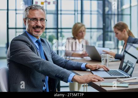 Uomo d'affari felice che indossa occhiali da vista seduto con un computer portatile Foto Stock