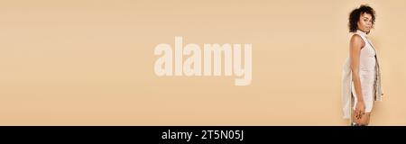 banner autunnale, splendida donna afroamericana in posa con un abito aderente con blazer su sfondo beige Foto Stock