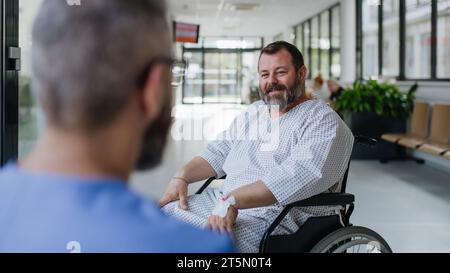 Primo piano del medico di supporto che parla con un paziente in sovrappeso preoccupato in sedia a rotelle. Malattie e malattie nella salute degli uomini di mezza età. Compassionevole Foto Stock