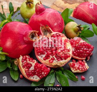 Frutti di melograno maturi con fette e foglie di melograno su una tavola di pietra grigia. Bella frutta sfondo esotico per i vostri progetti. Foto Stock